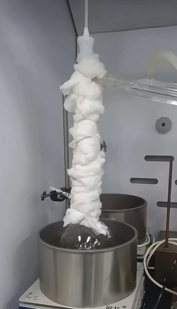 Glass Vigreux distillation column wrapped in white cotton insulation to prevent heat loss, connected to a round bottom flask in a heating mantle.