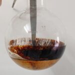 Round-bottom flask with severe caramelization and black tar at the bottom due to thermal runaway