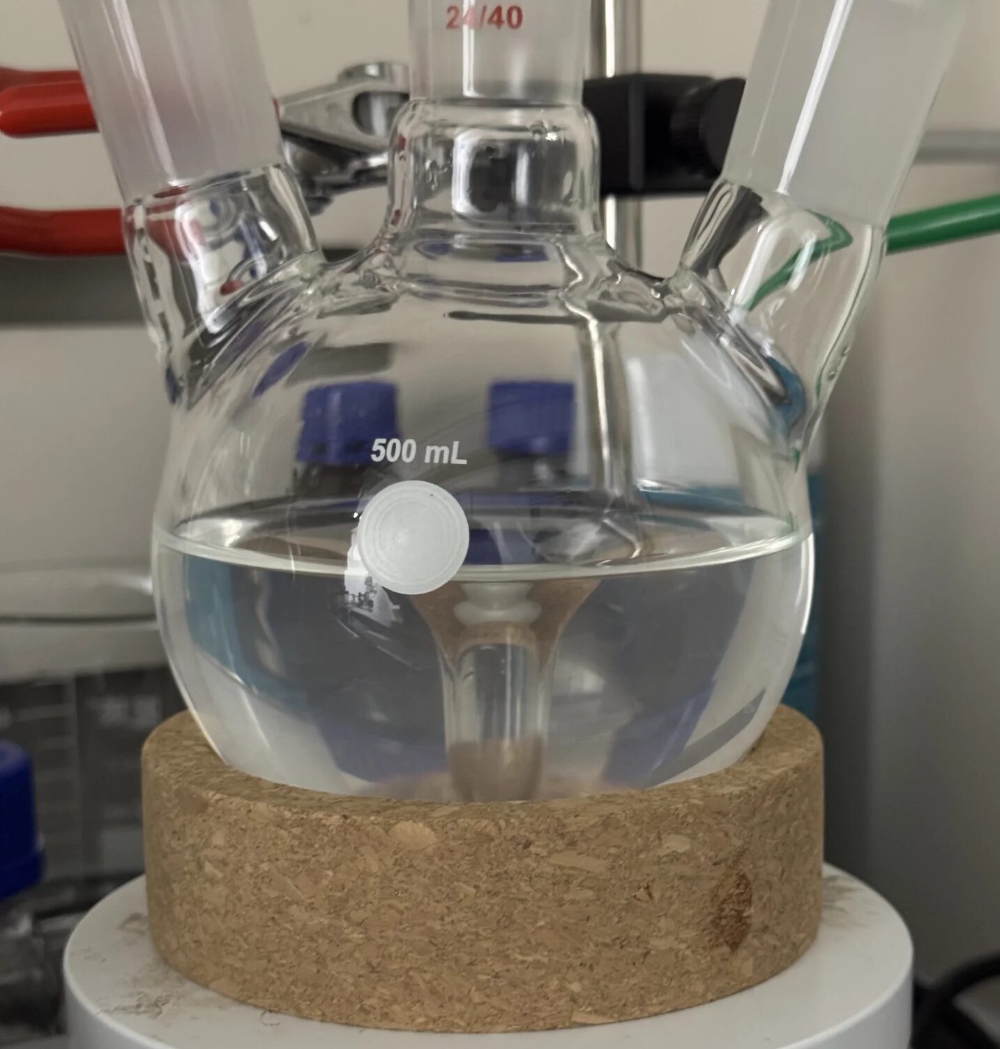Round-bottom multi-neck flask supported in a cork ring during setup, showing that a round-bottom vessel relies on external support rather than a self-standing base