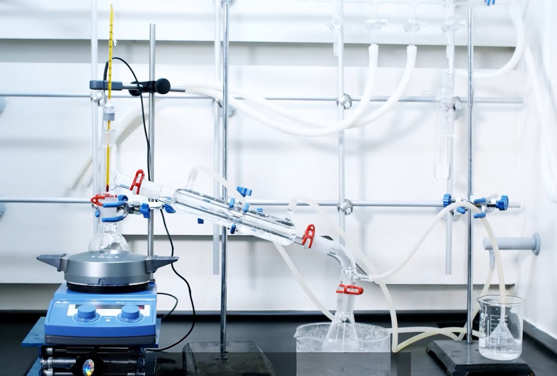 Simple distillation setup with heating mantle, thermometer, water-cooled condenser, receiving flask, and support stands on an organic lab bench